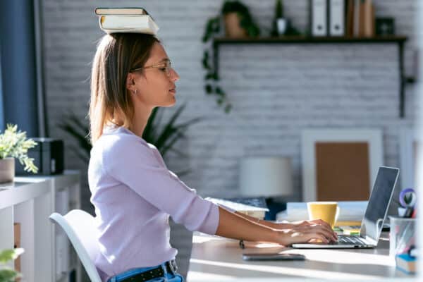 Young attractive woman at the desk with books on her head while working with computer at home.