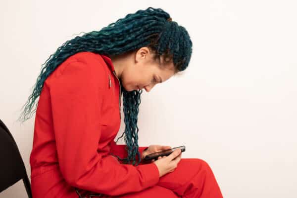 Woman with bad posture using smartphone while sitting on stool near light grey wall indoors, space for text