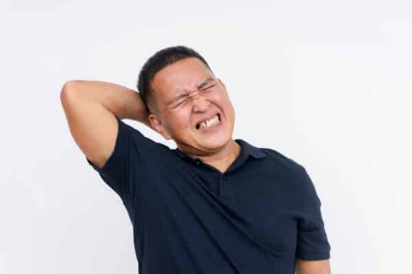 A middle-aged Asian man experiencing severe neck pain, depicting symptoms of whiplash, against a white background.